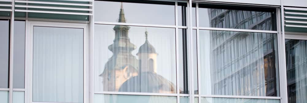 Das Bild zeigt die Spiegelung einer Kirche an der Glasfront eines Ordensspitals